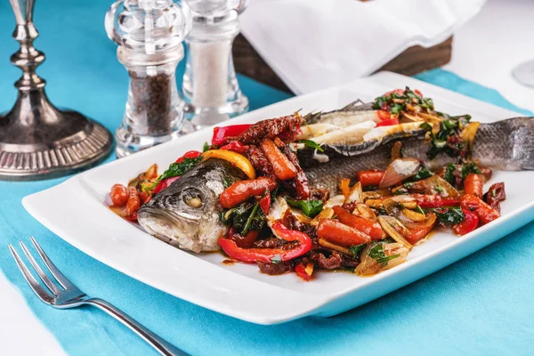 Seafood, Mediterranean cuisine, European dish. Whole fish baked with tomatoes with onion rings, red and green peppers, chili peppers, greens and vegetables. Caucasian national cuisine