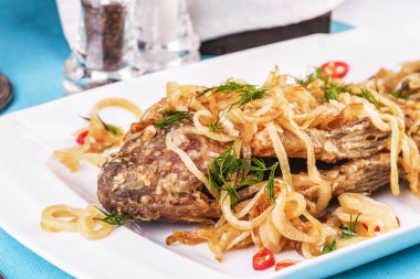 Kızarmış deniz balık turna levrek Gürcü tarifine göre soğan halkaları, biber ve yeşillik altında servis edilir. Akdeniz Mutfağı