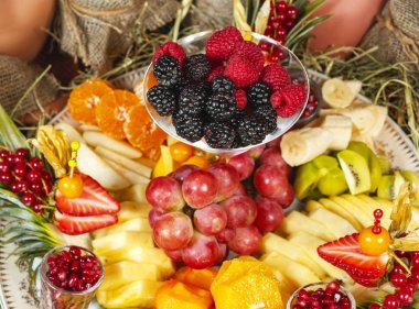 Gürcü tarzında meyve tabağı. Dilimlenmiş meyveler - elma, muz, ananas, portakal, armut, üzüm, hurma, çilek, ahududu, böğürtlen, pudra şekeri yaban mersini ile servis