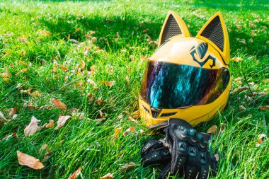 Aynalı, kulaklı, siyah motorcu eldivenli, motosikletli sarı motosikletli bir kız kaskı sonbaharda gri bir motosikletin arka planında yeşil çimlerde uzanıyor..