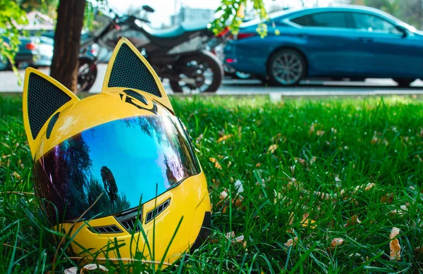 Un casco amarillo de una motocicleta con espejo de vidrio y orejas se encuentra en la hierba verde sobre el fondo de una motocicleta y coches en otoño . — Foto de Stock