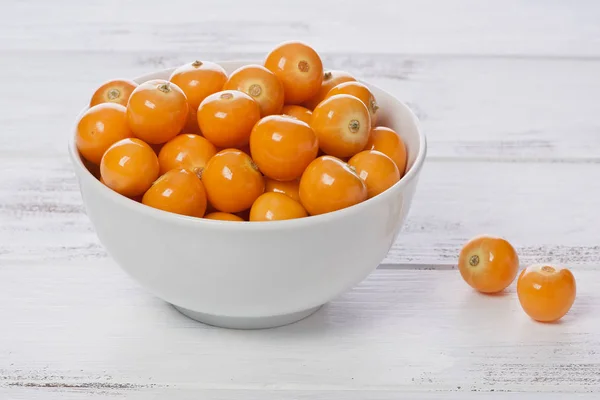 Several Cape Gooseberries, or goldenberries, in a white bowl with a painted white background.