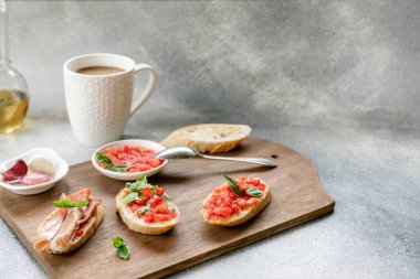 Bruschetta, dilimlenmiş domatesli tost, ahşap kesim tahtasında jamon ve fesleğen ve beyaz bardakta sütlü kahve. Boşluğu kopyala