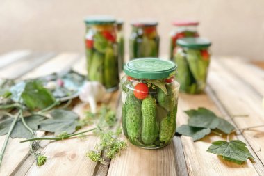 Tahta bir masada ve cam kavanozlarda dereotu, sarımsak ve baharatla konserve ve turşu yapmaya hazır taze salatalıklar.