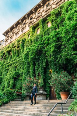 Milan, İtalya - 24 Mayıs 2018: A Milanese adam giymiş bir takım elbise yürüme aşağı Viale Luigi Majno yaprakları, Lombardiya, İtalya kaplı bir sarayda