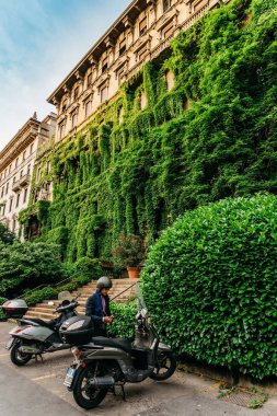 Milan, İtalya - 24 Mayıs 2018: yaprakları, Lombardiya, İtalya onun vespa Viale Luigi Majno sarayda önünde yanında bir takım elbise giymiş bir Milanese adam kaplı
