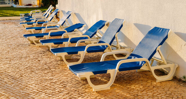 Blue plastic lounge chairs on cobblestones with soft summer sunshine
