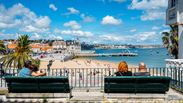 Two couples relax on a beach overlooking Praia da Ribeira on a sunny warm day