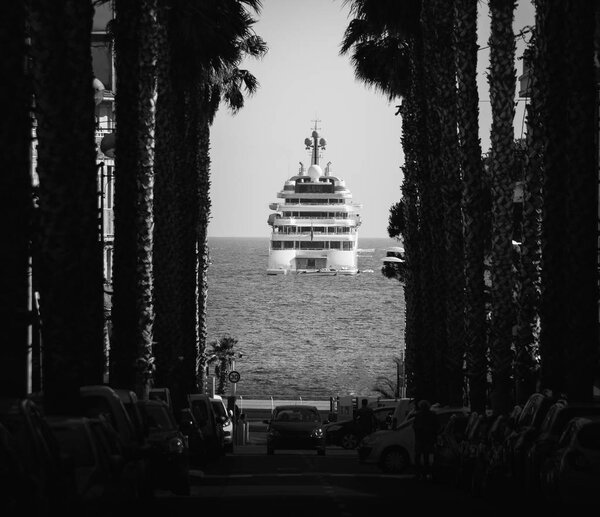 Monochrome palm tree lined boulevard with luxury yacht at end, captured in Juan les Pins, Cote d'Azur, France