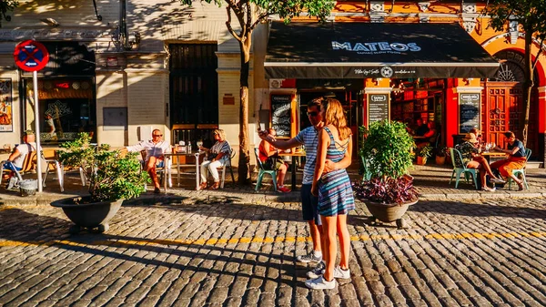 Pareja captura un selfie en una calle empedrada con terrazas de restaurantes en el centro histórico de Sevilla — Foto de Stock