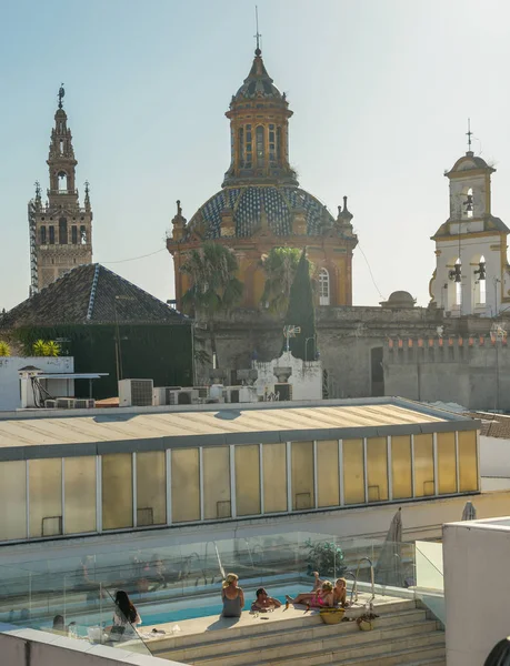 Un hombre afortunado y cinco mujeres disfrutan de un chapuzón en una piscina en la azotea con algunas bebidas alcohólicas con vistas al horizonte de Sevilla — Foto de Stock