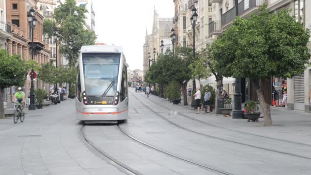 Tram électrique sur Constitution Avenue avec la cathédrale emblématique de Séville en arrière-plan. Piétons, cyclistes et hommes sur patins — Video