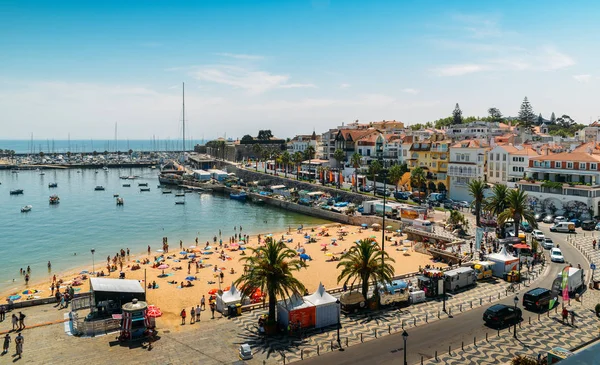 High vantage point of crowded sandy Praia do Ribeiro and boats on bay a a sunny summer day. Cascais is a small quaint village 30km west of Lisbon — Stock Photo, Image