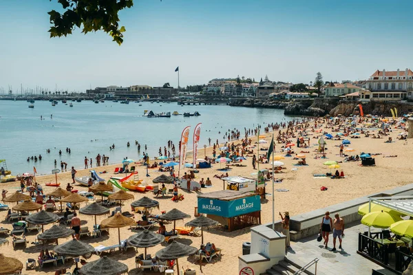 Cascais şehir antik kale de dahil olmak üzere arka planda ile bir sıcak yaz gününde Duquesa plaj kalabalık — Stok fotoğraf