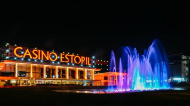 Facade of the Casino Estoril with colourful fountain show at night. Casino Estoril is one of the largest casinos in Europe and inspiration for Ian Flemings Casino Royale clipart