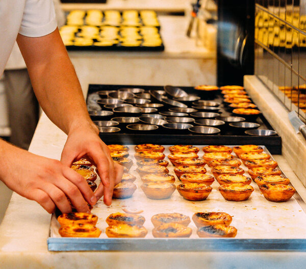 Worker organising rows of freshly cooked egg tart, traditional portuguese dessert, pastel de nata, custard tarts