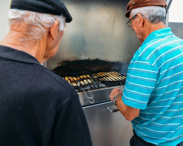 Двое португальцев жарят свежую рыбу, в том числе знаменитую бакальхау, на гриле в приморском городе Назаре, Португалия — стоковое фото