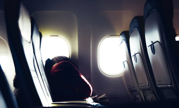 Müde lässige, nicht identifizierbare junge Frau aus dem kaukasischen Raum, die auf dem Sitz schläft, während sie im Flugzeug mit hellem Licht durch Fenster reist - Flugreisekonzept — Stockfoto