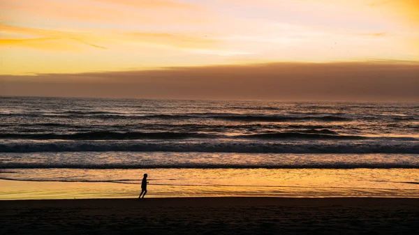 Silhueta de pessoa correndo na praia em Caparica, perto de Lisboa, Portugal ao pôr do sol — Fotografia de Stock