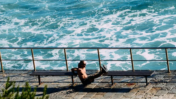 Middle aged athelete man exercises shirtless in between benches using his own weight. Waves crashing in background — Stock Photo, Image