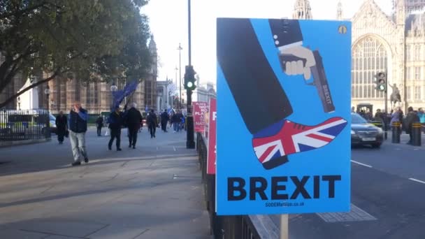 Anti-Brexit plakat utanför, Westminster, London, Uk föreställande Brexit som skjuter Storbritannien i foten på en blåsig dag — Stockvideo