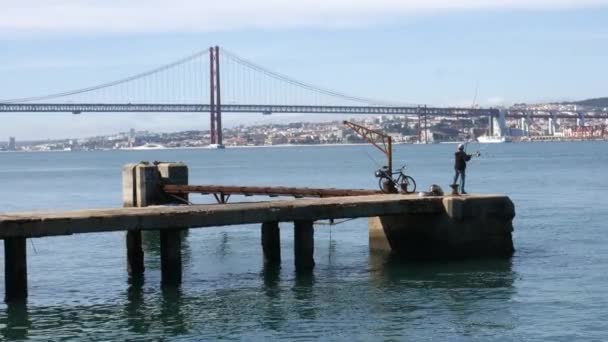 Jediný rybář na Tagus, s výhledem na historické 25 dubna most na řece Tejo — Stock video