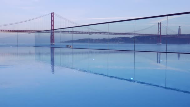 Západ slunce nad 25 dubna most v Lisabonu, Portugalsku s odrazem od nekonečný bazén — Stock video