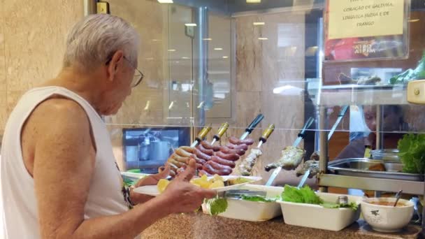 Un homme plus âgé avec des lunettes est servi un saumon barbecue tandis que dans un restaurant buffet — Video