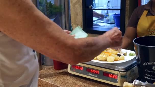 Older man puts his food on a machine that weighs and gives a receipt — Stock Video