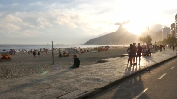 Vue panoramique du coucher de soleil doré sur la plage d'Ipanema avec piétons et cyclistes le long de la promenade - 4K — Video