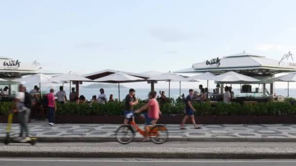 Quiosco ocupado en la playa de Ipanema con peatones y ciclistas a lo largo de la acera en Río de Janeiro, Brasil — Vídeos de Stock