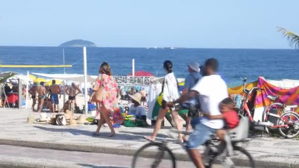 Двое мужчин продают шляпы и пляжные аксессуары туристам на знаменитом пляже Ипанема в Рио-де-Жанейро — стоковое видео