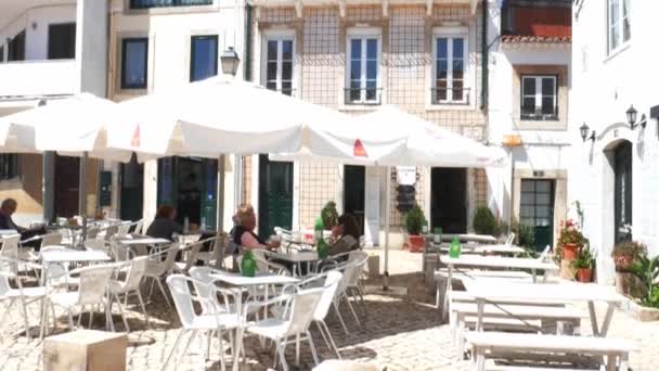 Mensen ontspannen genieten van een café op een terras in Cascais, Portugal met traditionele gebouwen op de achtergrond — Stockvideo