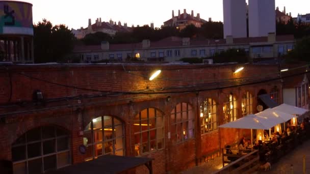 レストランのテラスで、日没時にポルトガルのリスボンの25 4月橋の底に向かってパンアップ。Lx工場、アルカンタラで撮影 — ストック動画