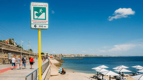 Señal de ruta de evaculación de tsunamis junto a un paseo marítimo con peatones en Cascais, Portugal — Foto de Stock