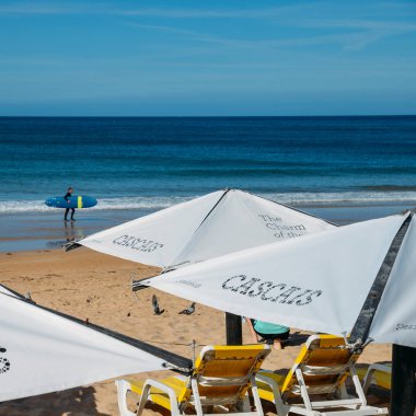 Cascais, Portekiz plaj şemsiyeleri ve şezlongile arka planda sörf