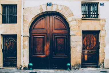 Çerçeveli kapı panelleri ve süslü metal kafesler tarafından korunan yuvarlak pencereler ile Vintage ahşap kapı. Paris Fransa'da antikçift kapı yaşlı ahşap yüzeyinde parlak pirinç kapı kolları. Simetri şekilleri