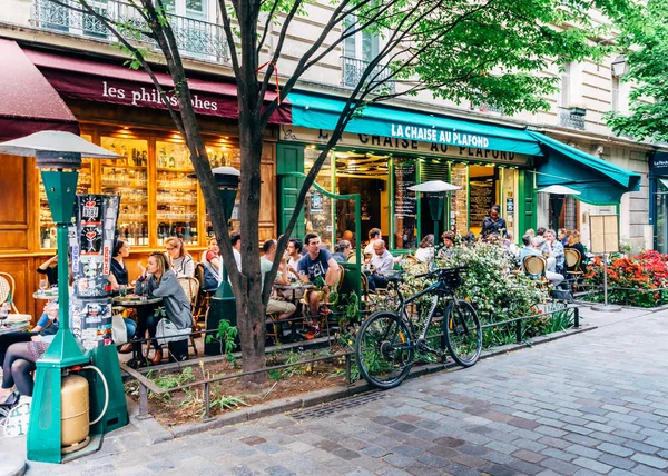 La gente disfruta de una cafetería y una conversación en una tranquila y encantadora calle arbolada en el bohemio barrio de Marais de París, Francia, durante la primavera. — Foto de Stock