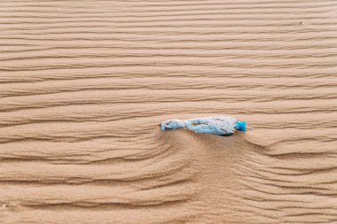 Desenleri ile bir kumul çölde oturan su kullanılmış bir plastik şişe