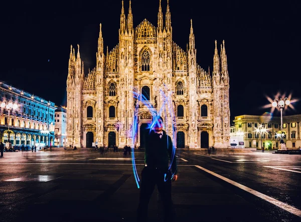 Man using light painting long exposure draws an M letter in front of the Milan Cathedral, Milan, Italy