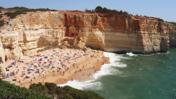 Hoog perspectief op goudkleurige kliffen, druk strand en turquoise Oceaan in Benagil Beach, Lagoa, Algarve, Portugal — Stockvideo