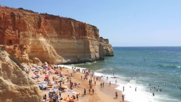 Hoog perspectief op goudkleurige kliffen, druk strand en turquoise Oceaan in Benagil Beach, Lagoa, Algarve, Portugal — Stockvideo