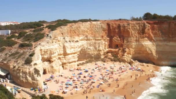 High perspective panning of gold-coloured cliffs, busy beach and turquoise ocean in Benagil beach, Lagoa, Algarve, Portugal — Stock Video