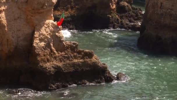 Bandera portuguesa en el viento en la bahía de Ponta da Piedade que consta de impresionantes formaciones rocosas en la región del Algarve de Portugal — Vídeo de stock