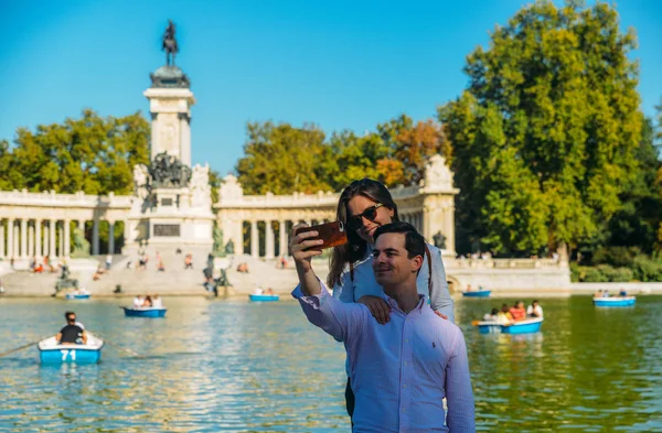 Pareja toma un selfie frente a embarcaciones frente al monumento a Alfonso XII en el Parque del Buen Retiro, Madrid, España — Foto de Stock