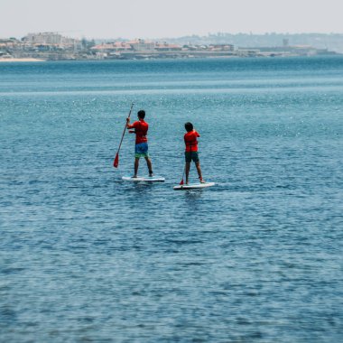 Cascais, Portekiz - 28 Temmuz 2020: Yazın Cascais Körfezi 'nde ayakta kürek çeken ve arka planda Estoril kıyı şeridi bulunan insanlar