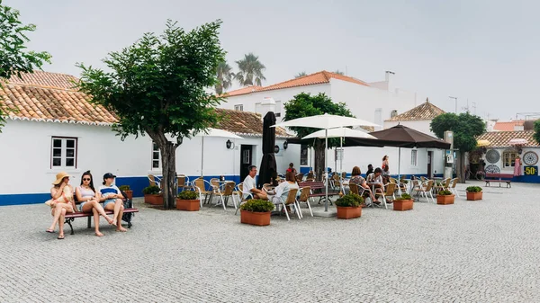Praça principal com pessoas relaxantes em cafés na pitoresca Porto Covo em Portugal — Fotografia de Stock