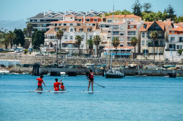 Cascais, Portugal - 28 de julio de 2020: Las personas que disfrutan de stand up paddle en Cascais Bay durante el verano con la costa de Estoril en el fondo — Foto de Stock