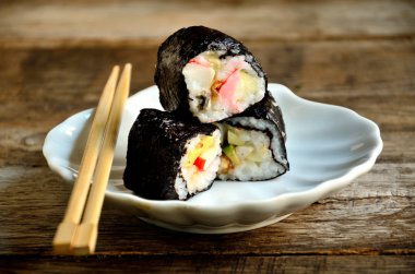 Eski ahşap bir masa üzerinde beyaz bir tabakta suşi ve yemek çubukları.