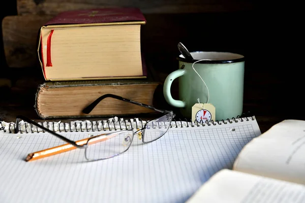 Squared notebook, pencil, glasses, old books and a mug with tea.